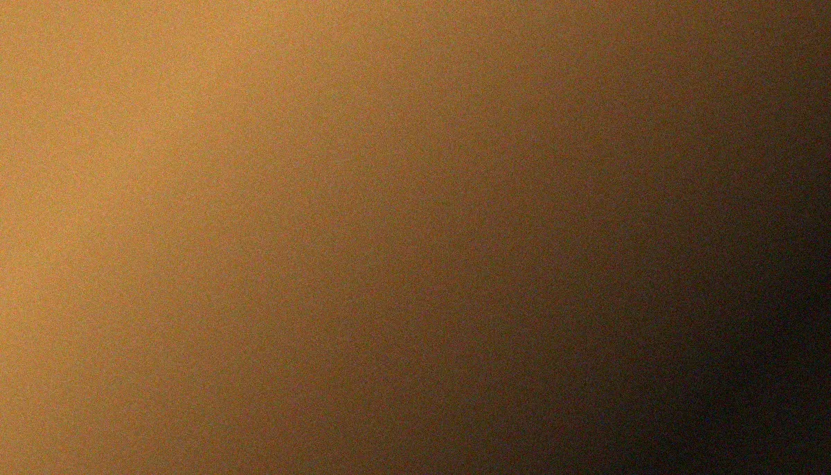 A warm mesh gradient pools muted amber and dusty gold across the upper-left of the frame, sweeping diagonally through brown and taupe into deep charcoal at the lower-right corner, the soft arc suggesting the curve of a dial, the whole image veiled in heavy film grain.